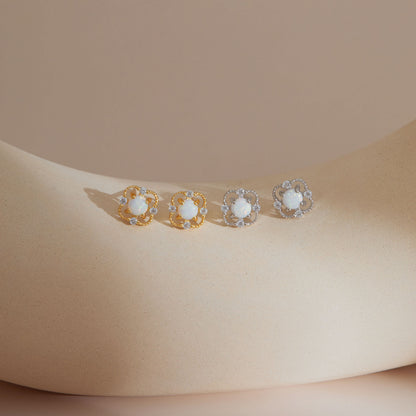 Gold and silver faux opal floral stud earrings displayed on a soft curved surface in warm natural light