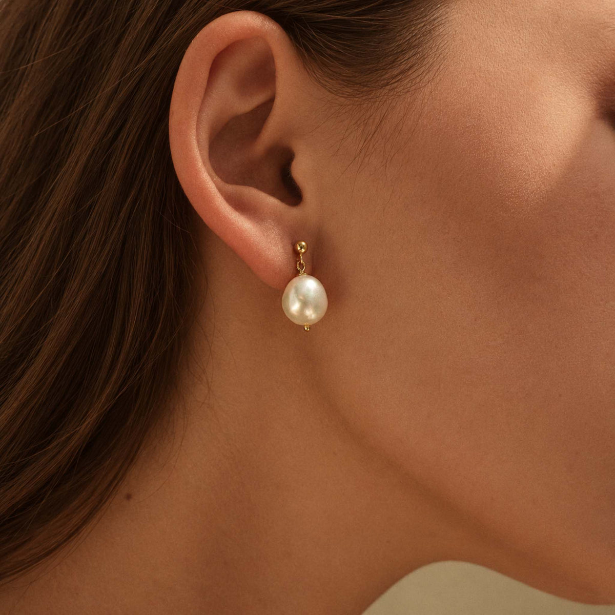 Close-up of an ear wearing a baroque freshwater pearl drop earring with a small gold ball stud on the lobe