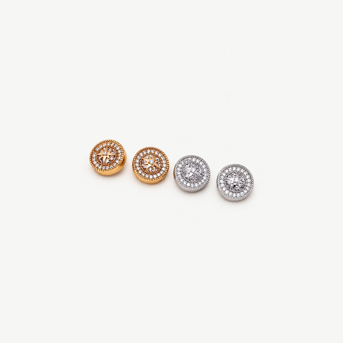 Two pairs of starburst halo stud earrings, gold-plated and sterling silver, set in a diagonal row on off-white