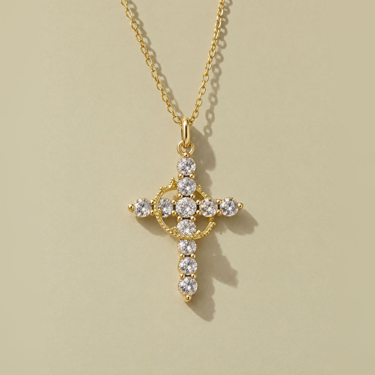 Gold plated crown cross pendant with clear cubic zirconia and a rotating crown ring, laid flat on pale khaki