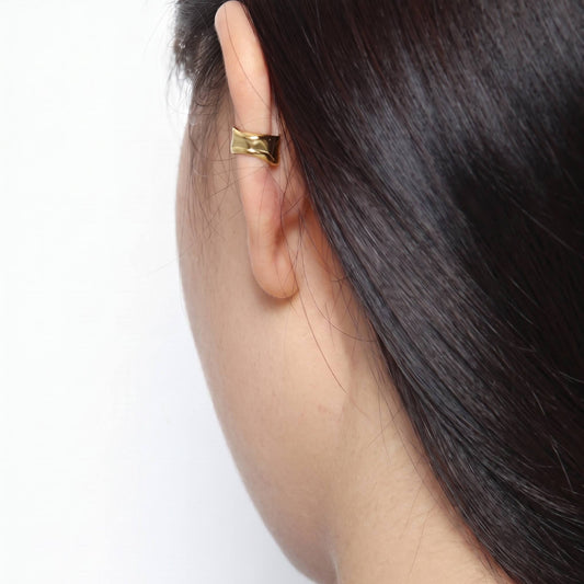 Small gold ear cuff worn high on the helix without a piercing, shown against dark hair