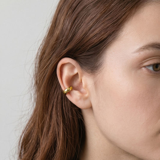 Woman wearing a gold-plated dome ear cuff on the middle of her ear, close side view with long brown hair