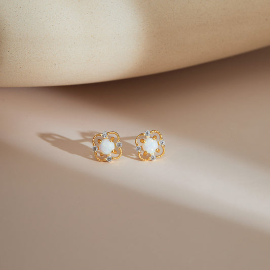 Gold S925 floral opal stud earrings resting on a soft neutral surface