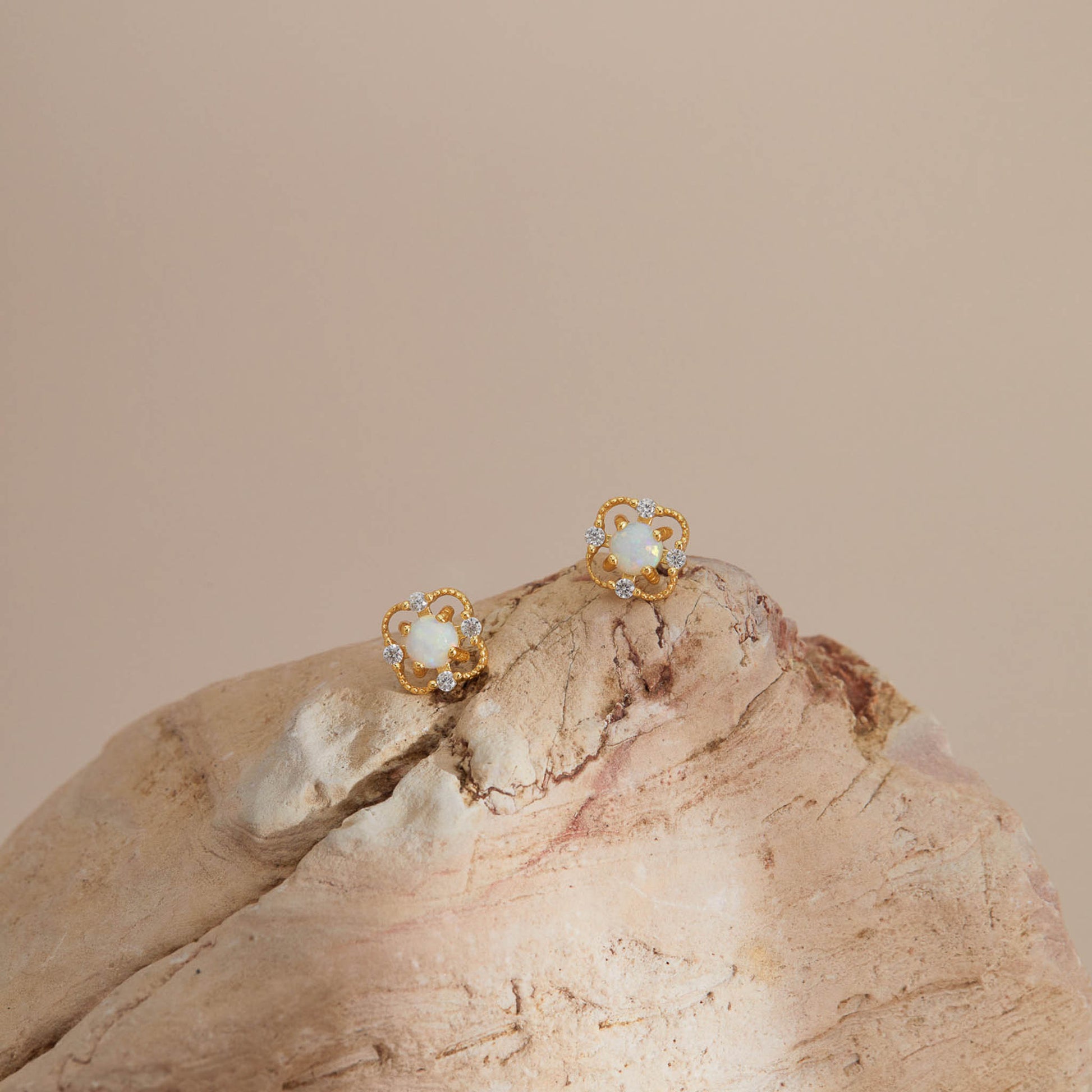 Gold opal floral stud earrings styled on textured stone for a warm, natural look