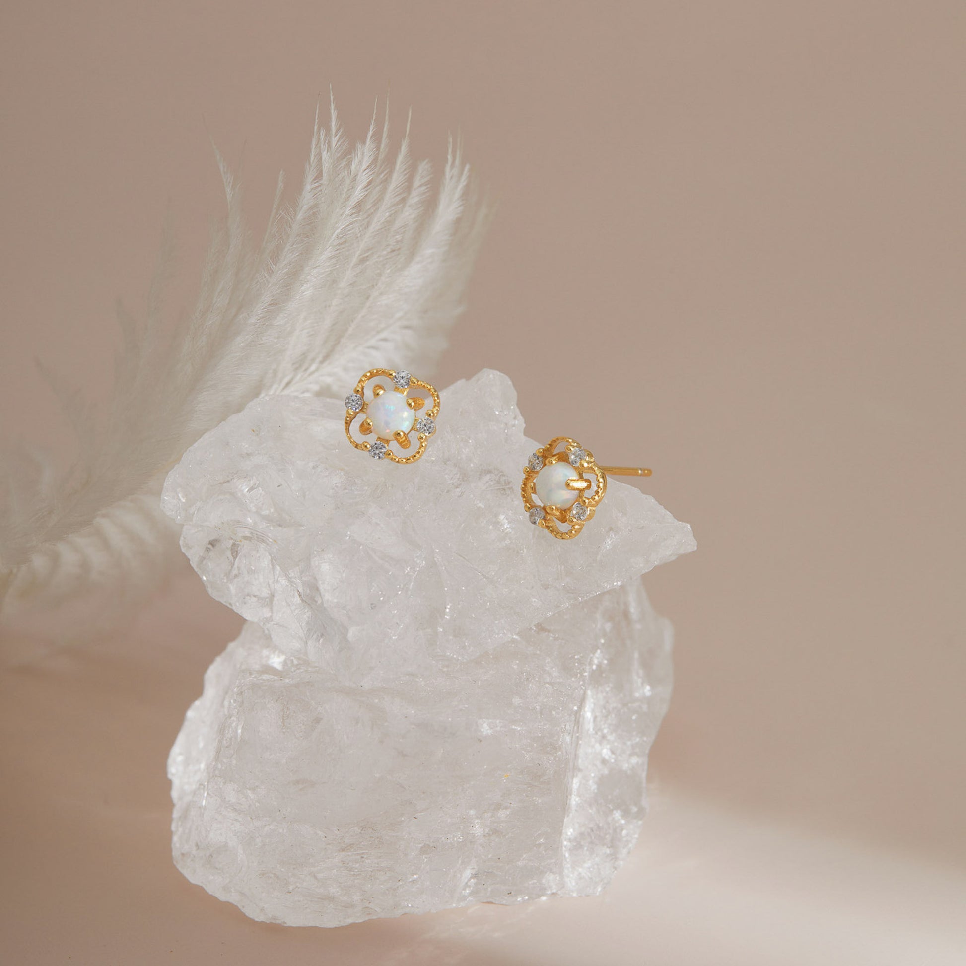 Gold S925 floral opal studs displayed on clear crystal with soft light.