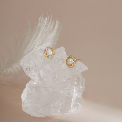 Gold S925 floral opal studs displayed on clear crystal with soft light.
