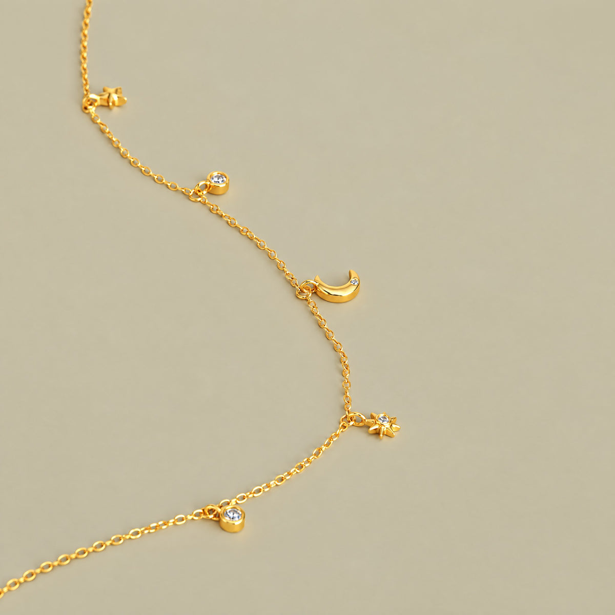 Close up of gold plated crescent moon, starburst and bezel set round stone charms on a pale khaki backdrop