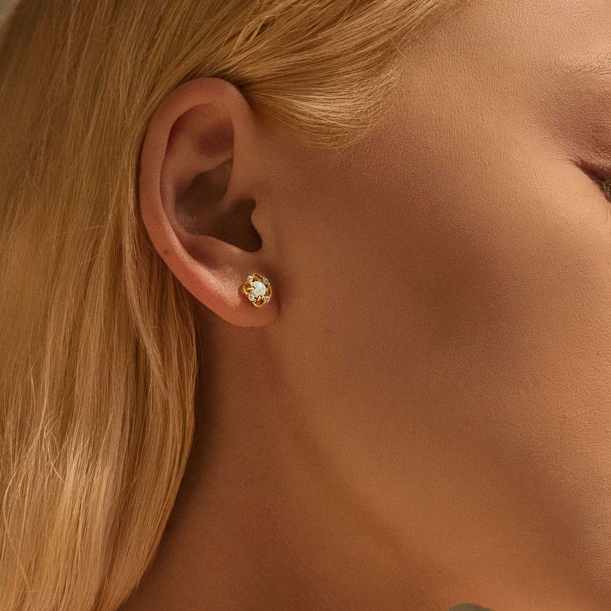 Gold floral opal stud earring worn on ear, soft natural lighting