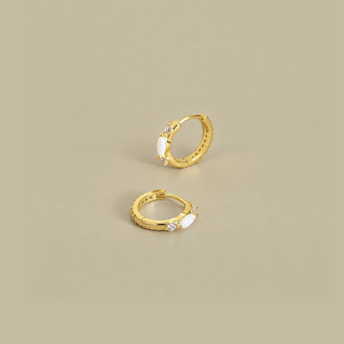 Gold plated opal huggie hoops on a pale khaki backdrop, one standing to show the cubic zirconia band, one lying flat
