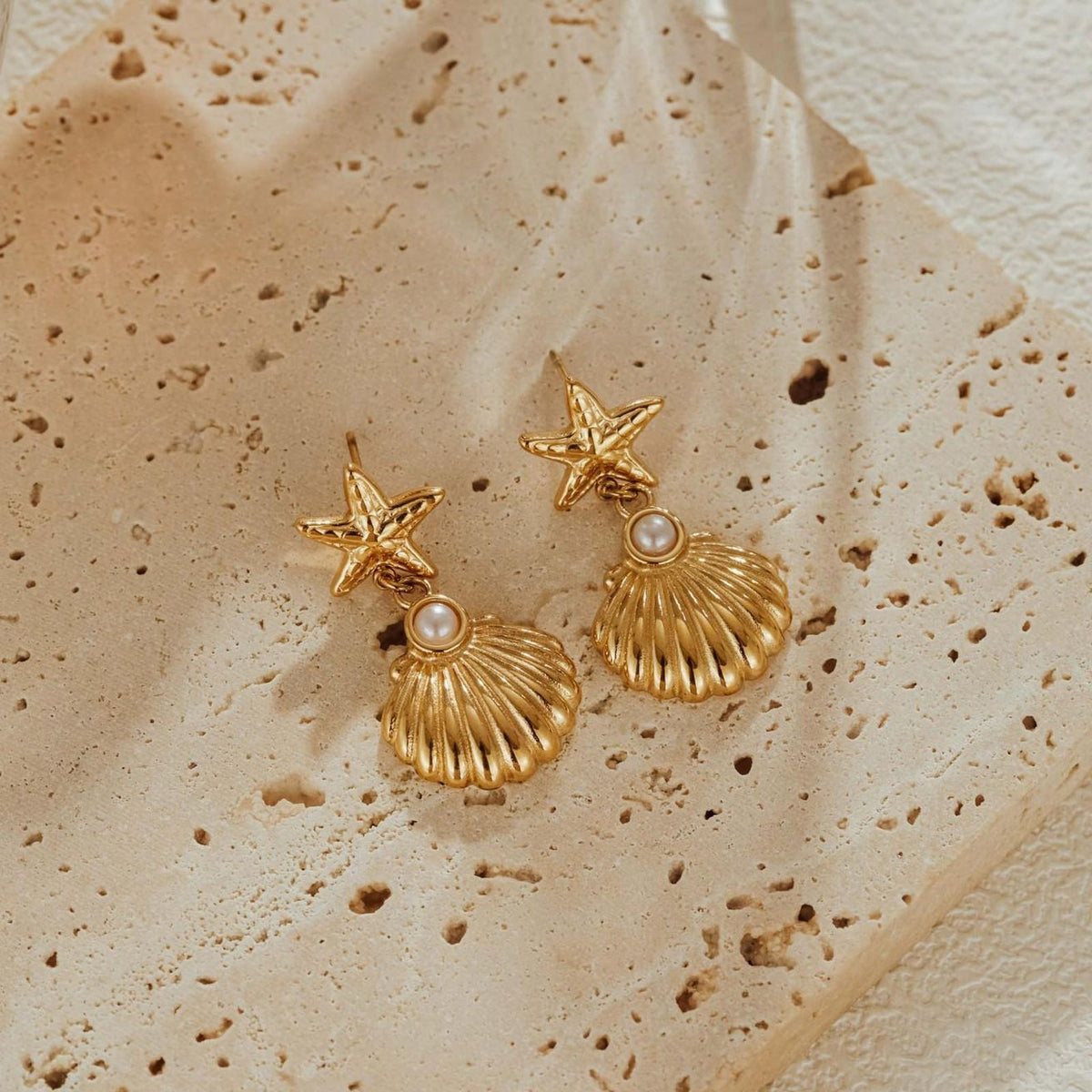 Pair of 18k gold plated starfish and scallop shell drop earrings with shell pearls on pitted travertine stone