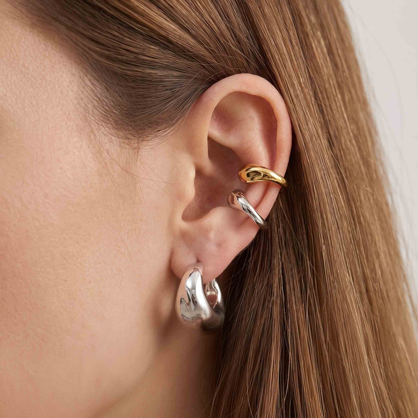 Woman wearing gold and silver ear cuffs stacked on the upper ear without a piercing