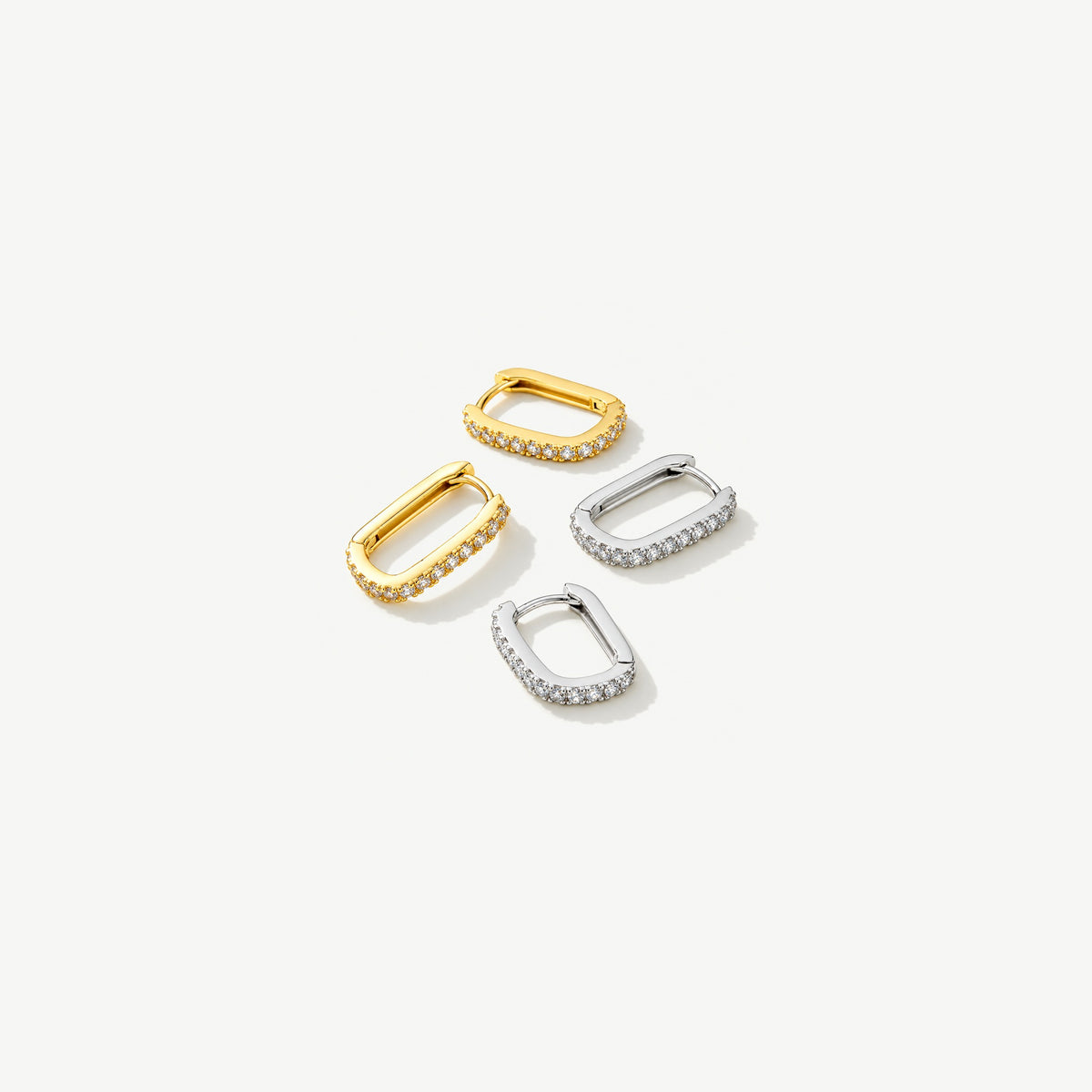 Two gold plated and two sterling silver U hoop huggie earrings lying flat, a row of small stones along each base