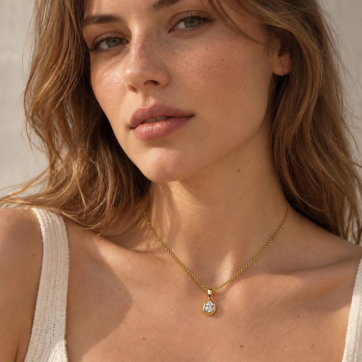 Woman with long wavy hair in a white knit tank top wearing a dainty 14k gold plated teardrop pendant necklace