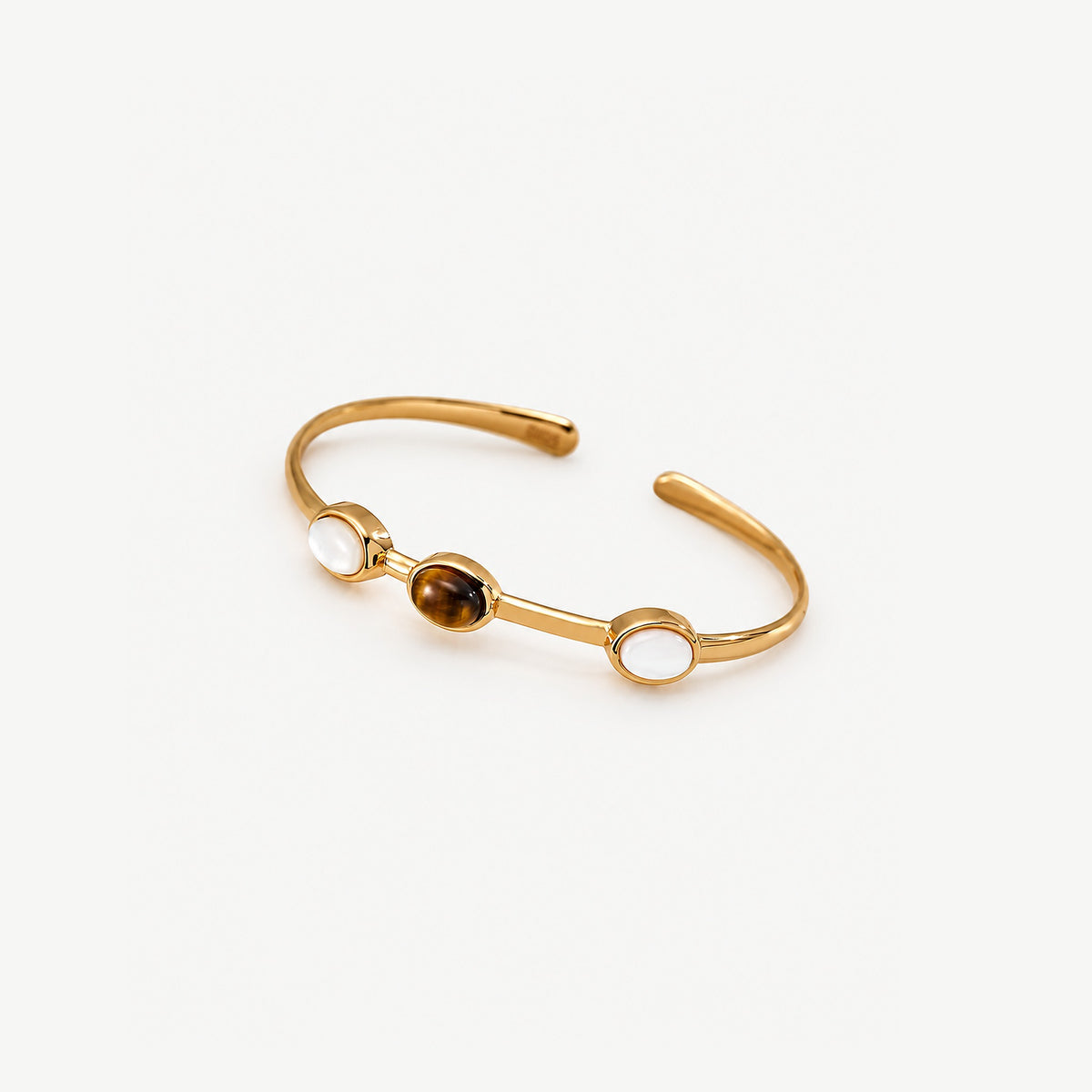 Gold tiger eye cuff bracelet in three-quarter view, the stone between two white ovals on a slim open band