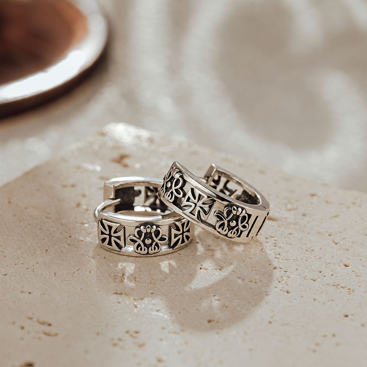 Oxidized sterling silver gothic huggie earrings with heraldic cross and fleur-de-lis engraving on stone surface