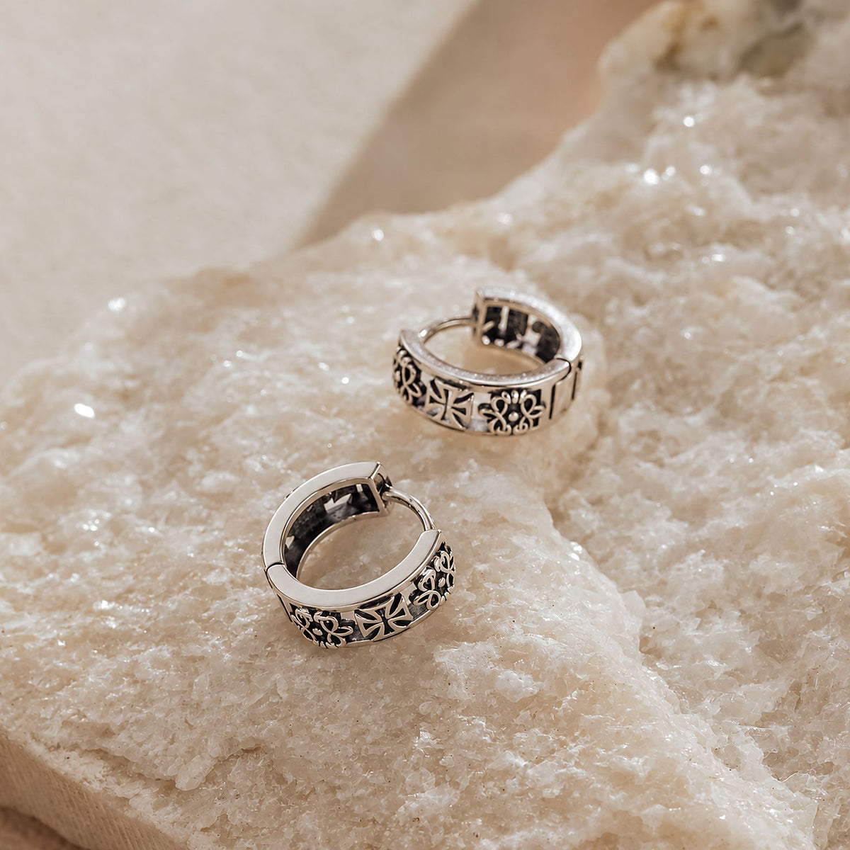 Pair of sterling silver gothic huggie earrings on white quartz surface