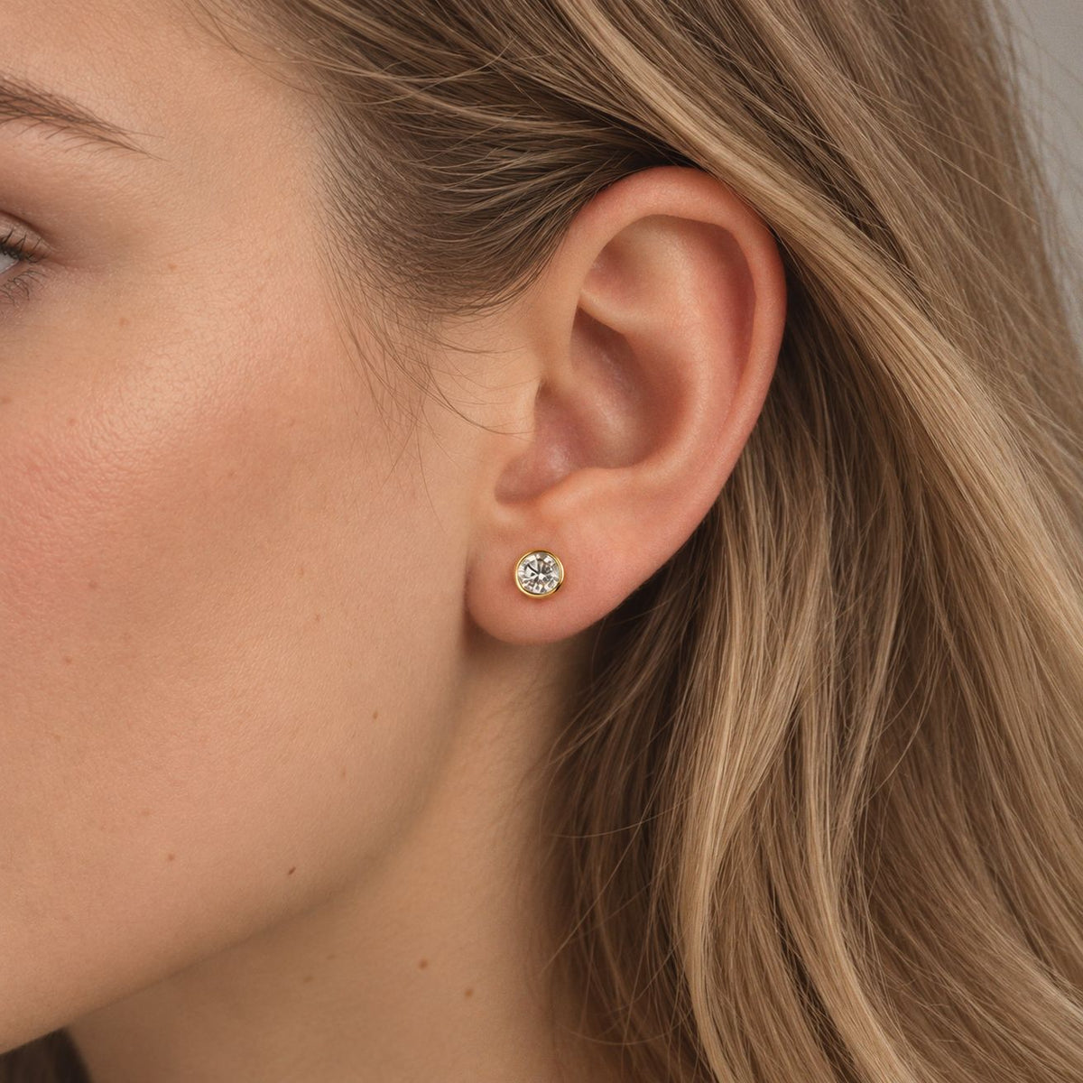 0.5 ct gold bezel moissanite stud earring worn on the earlobe, close-up of a woman with long blonde hair