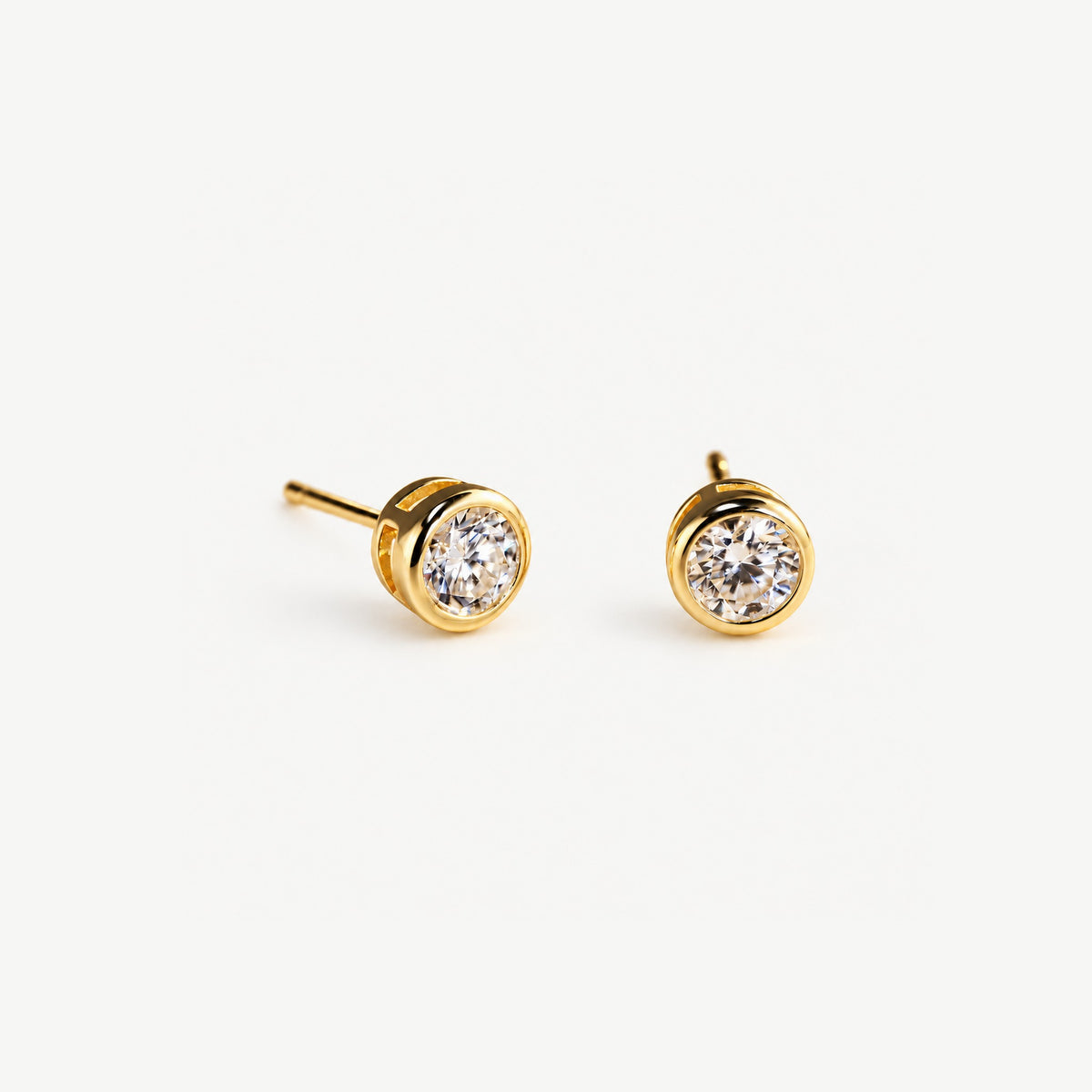Pair of 0.5 ct moissanite stud earrings in 14k gold plated bezels, angled view with posts on a light ground
