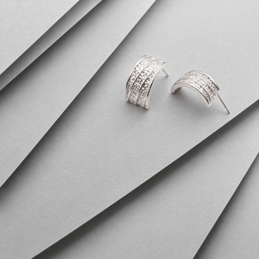 Chunky sterling silver hammered half hoop earrings on layered grey card, one showing the ribbed front, one the arc