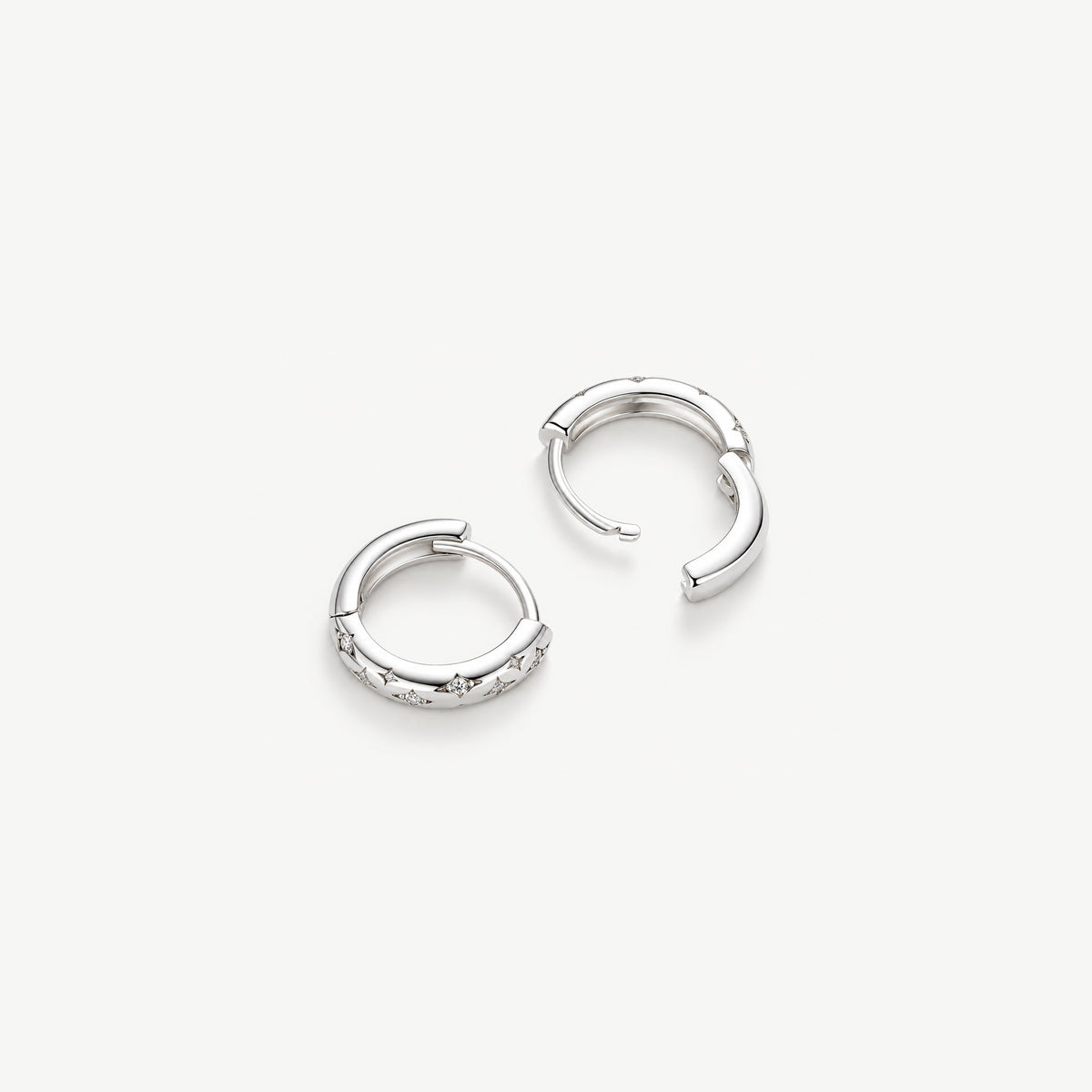Two sterling silver star huggie earrings, one open on its hinge to show the snap closure and inner band