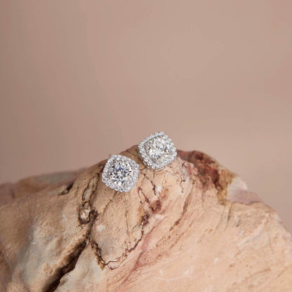 Flat lay on rock — White moissanite halo stud earrings, cushion setting.