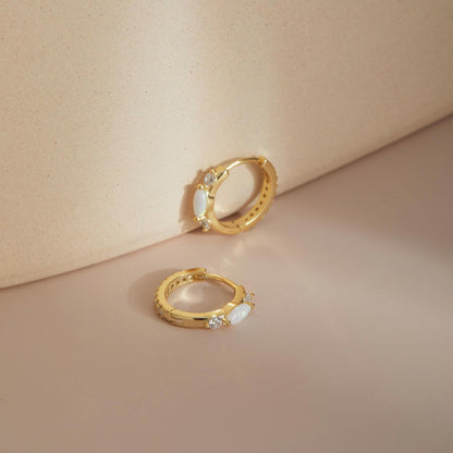 Gold opal huggie hoop earrings styled against soft backdrop