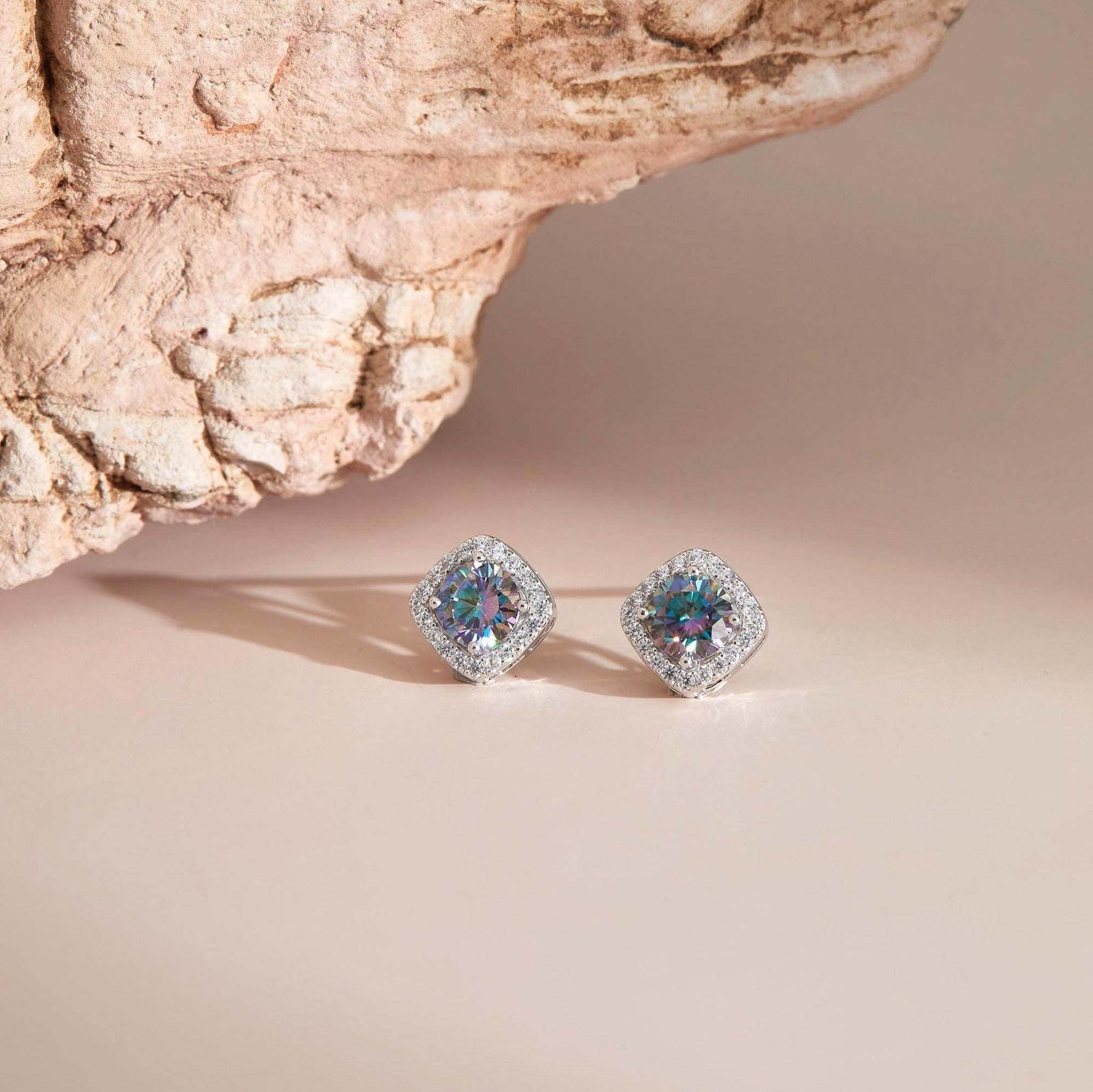 Flat lay on neutral surface — Rainbow blue moissanite halo stud earrings with sparkle.