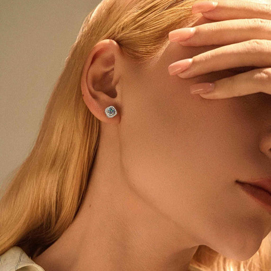 Woman with long blonde hair wearing a rainbow blue moissanite halo stud earring, hand raised across her face