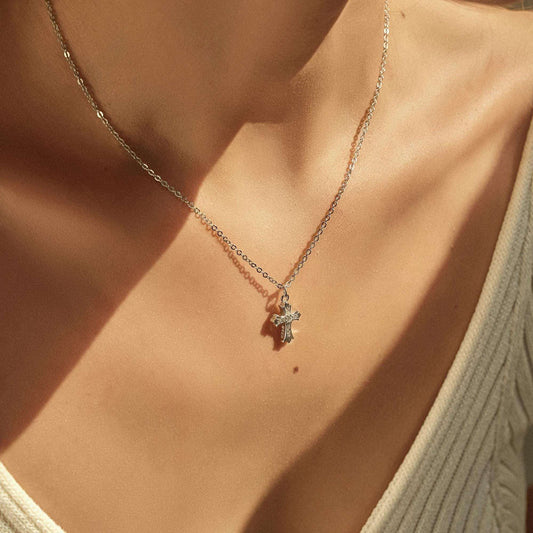 Necklace with a cross pendant on a person wearing a light green top.