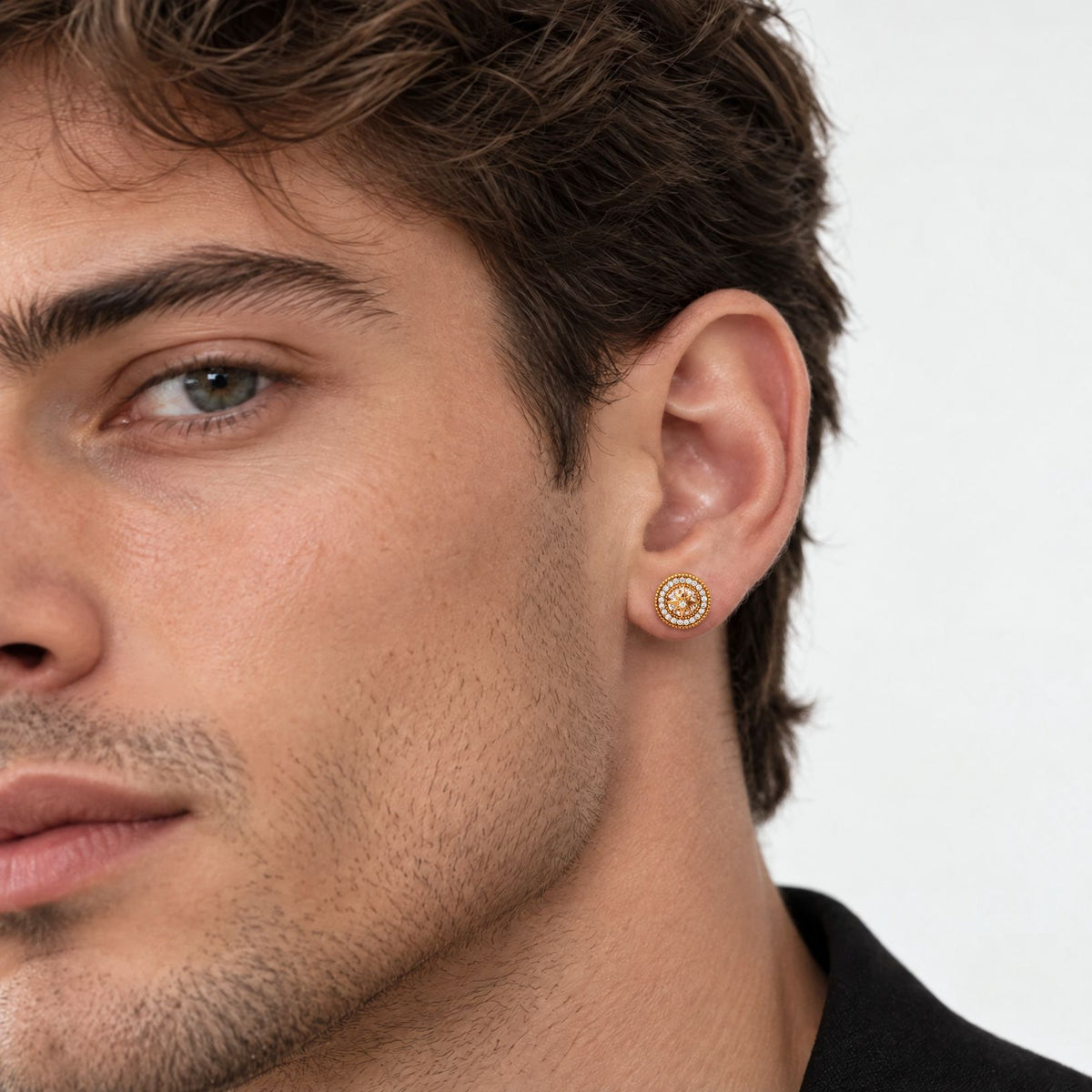 Man with short brown hair wearing a gold-plated starburst halo stud earring, close side view of half his face