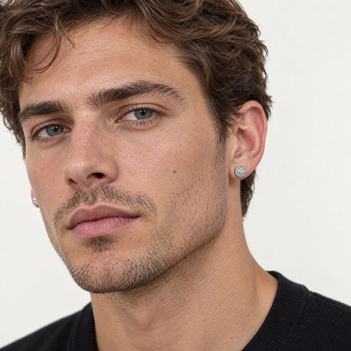 Man with wavy brown hair wearing a sterling silver starburst halo stud earring, three-quarter close-up of his face
