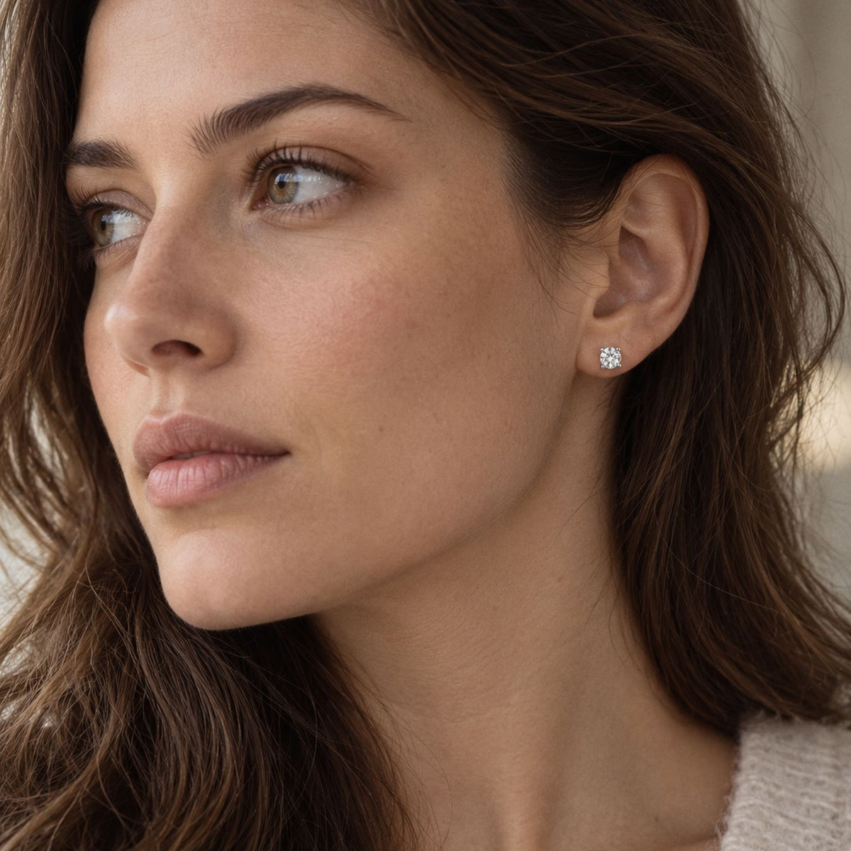 Brunette woman in a cream knit, face turned three quarters and looking away, wearing a sterling silver moissanite stud
