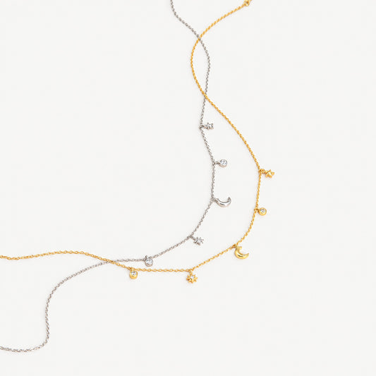 Gold plated and white gold plated moon and star charm necklaces crossing each other on a plain near-white background