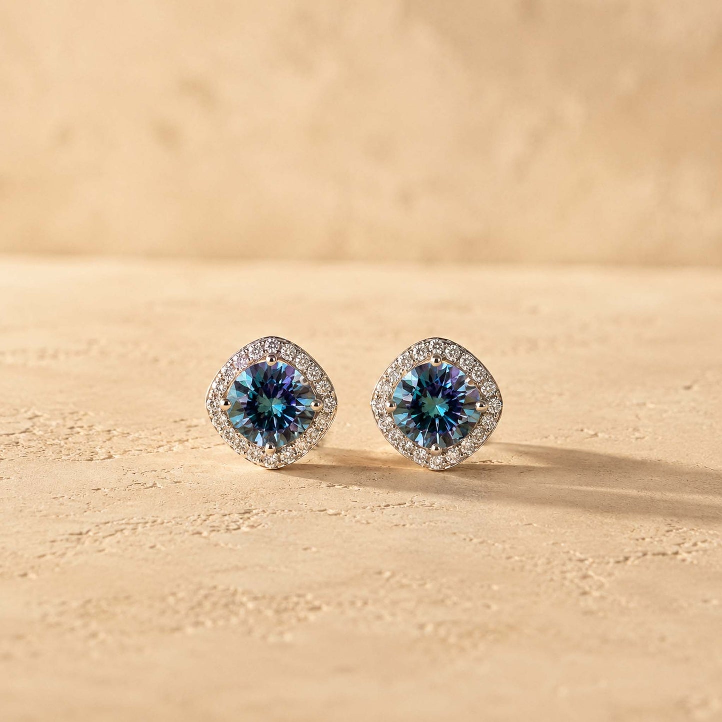 Pair of 1ct round cut rainbow blue moissanite halo stud earrings in sterling silver, warm afternoon light