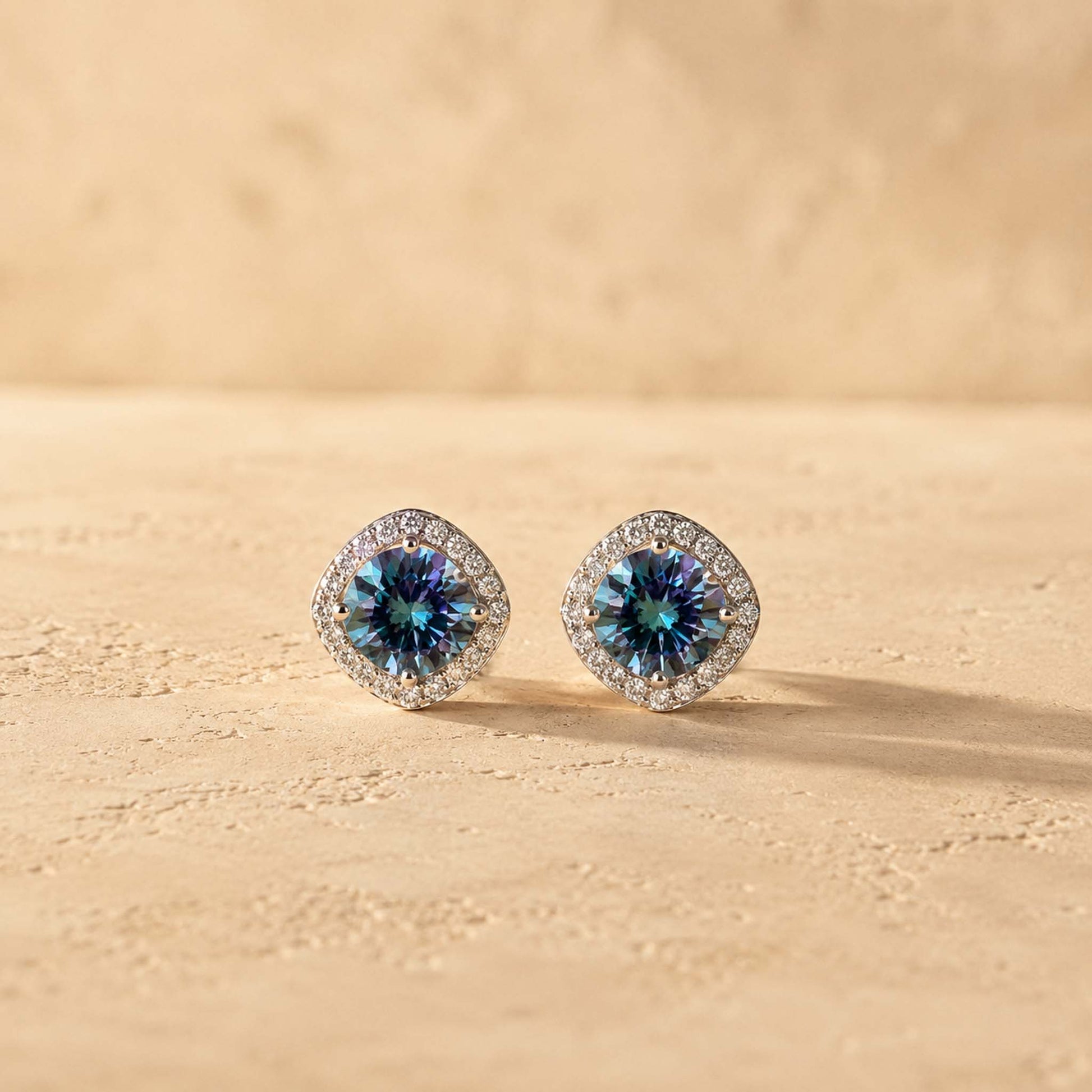 Pair of 1ct round cut rainbow blue moissanite halo stud earrings in sterling silver, warm afternoon light