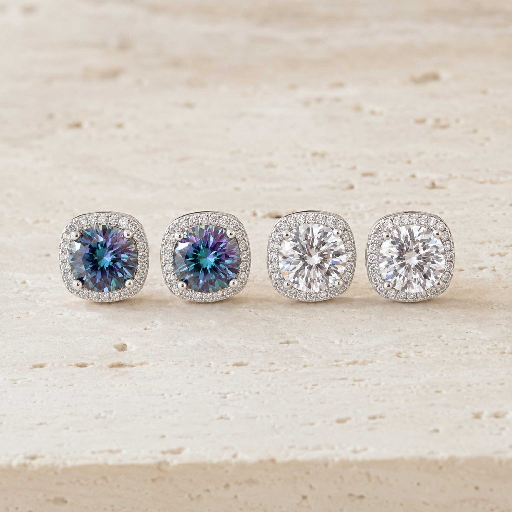 Two pairs of 1ct round cut moissanite halo stud earrings in sterling silver, rainbow blue and white, on travertine