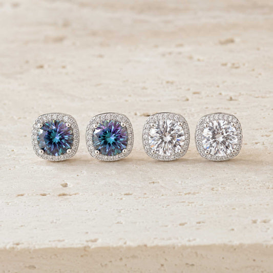 Two pairs of 1ct round cut moissanite halo stud earrings in sterling silver, rainbow blue and white, on travertine