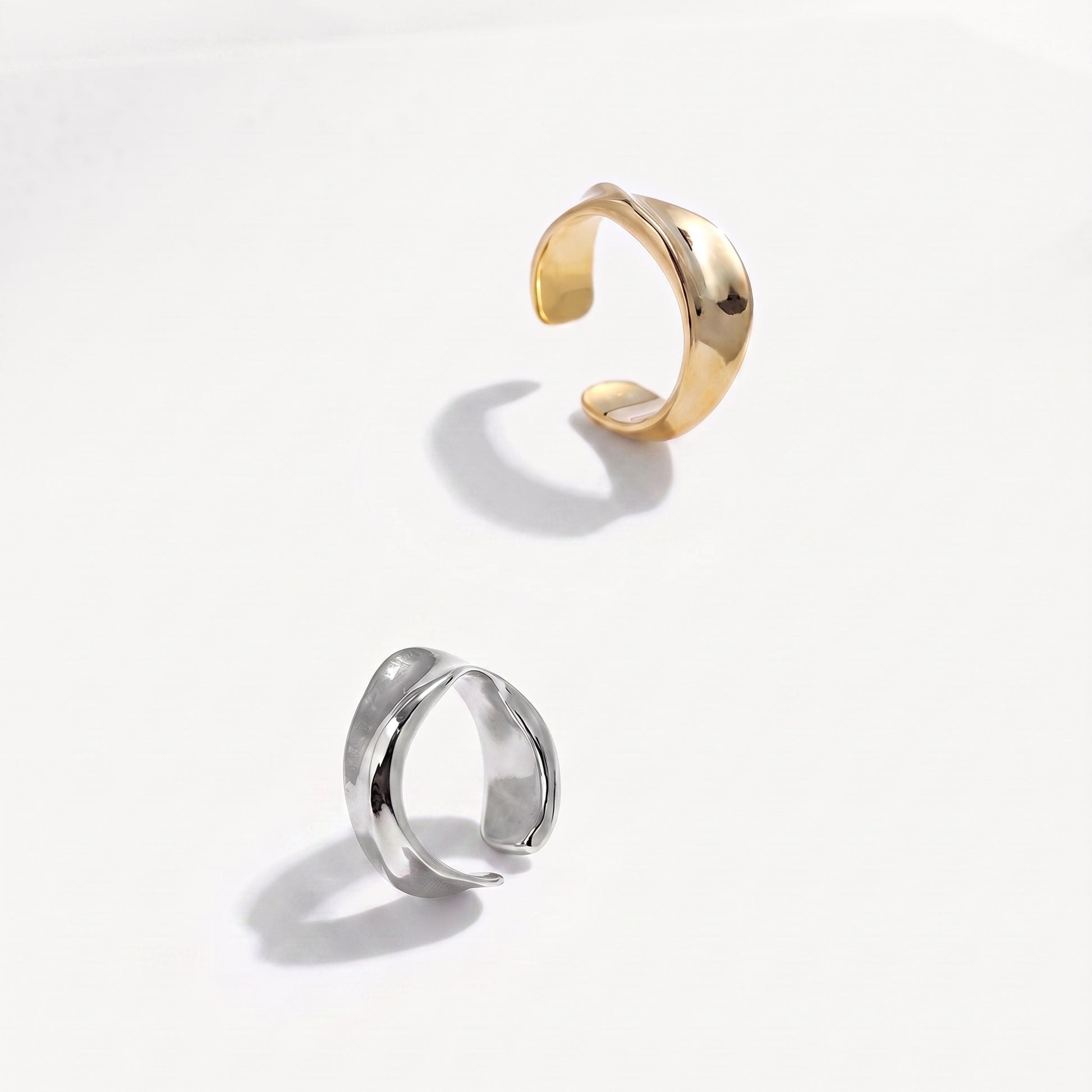 Gold and silver twisted ear cuffs at a high angle on a near-white ground, open bands facing up