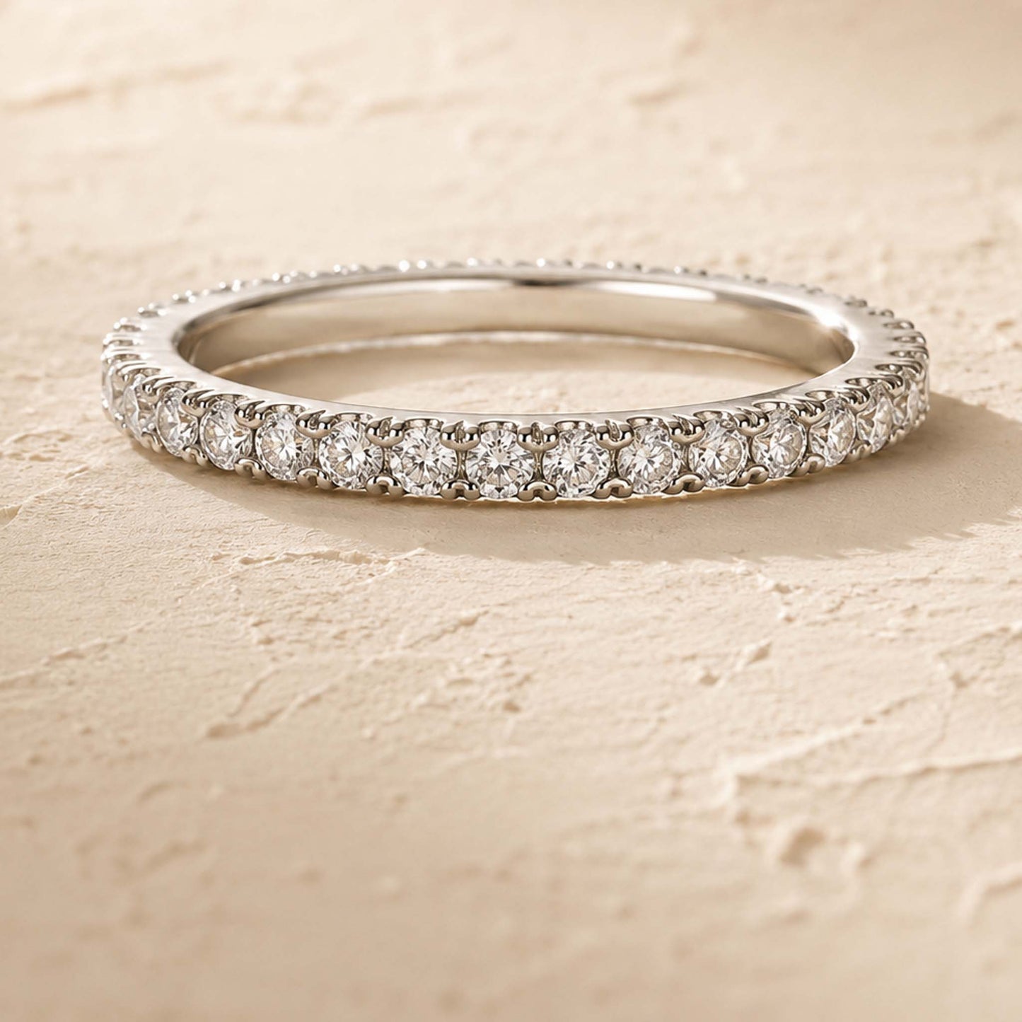 Sterling silver moissanite eternity ring with 31 pavé-set stones, top view on cream textured surface