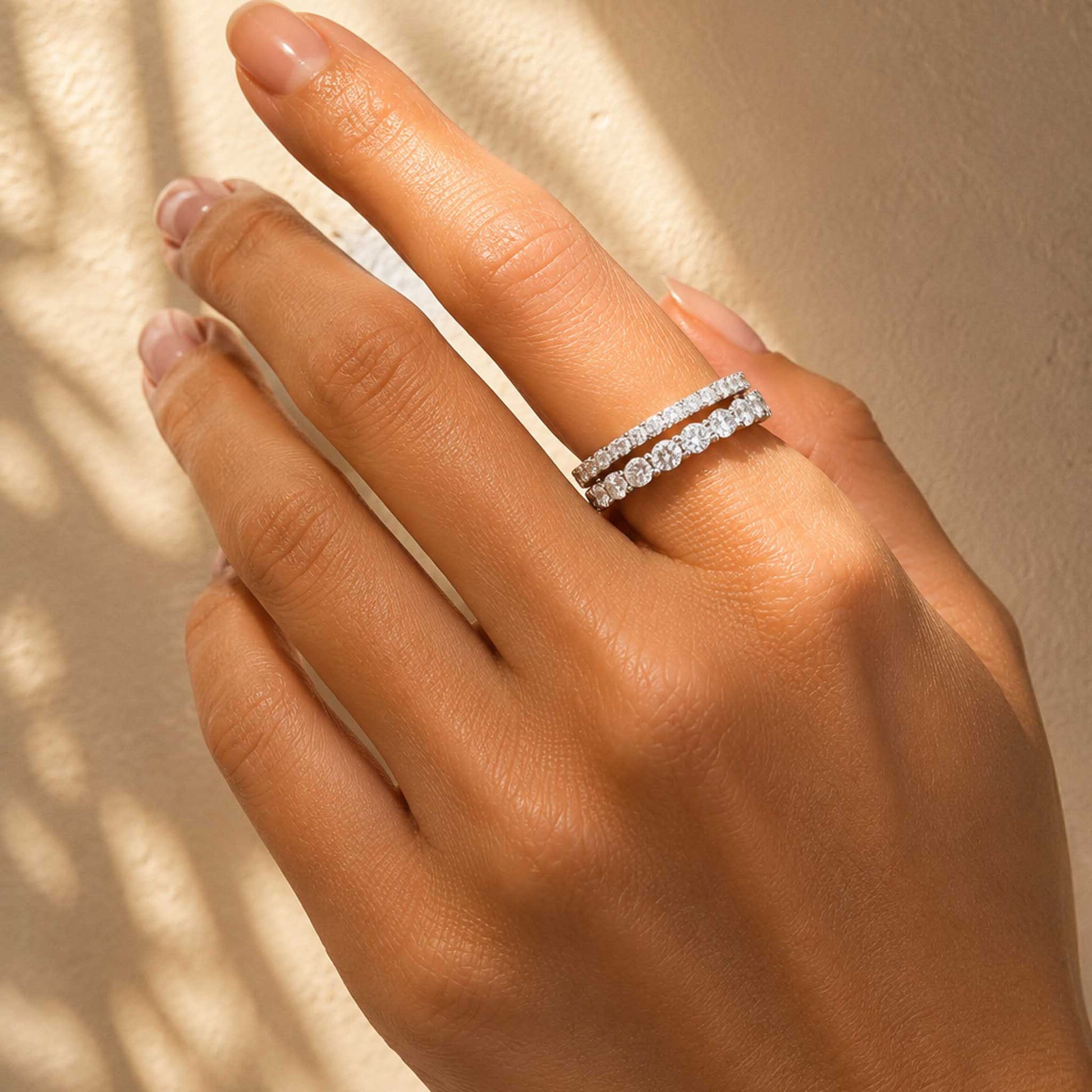 Sterling silver moissanite eternity ring stacked with another ring on hand in soft morning light