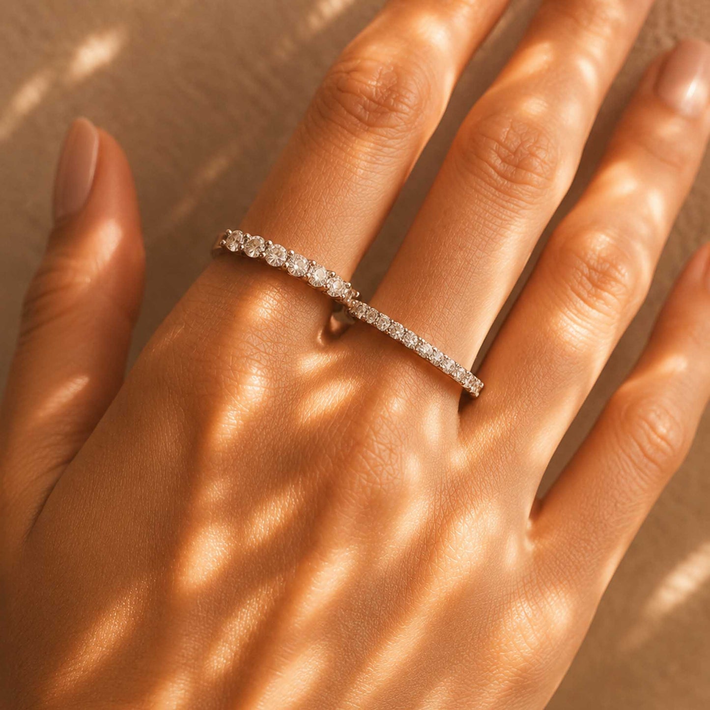 Sterling silver moissanite eternity ring worn on model's ring finger, styled stacked with another ring in sunlight