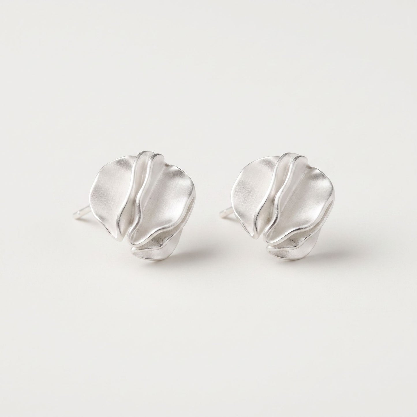 Sterling silver petal stud earrings tilted forward, showing the folded ridges and brushed satin finish