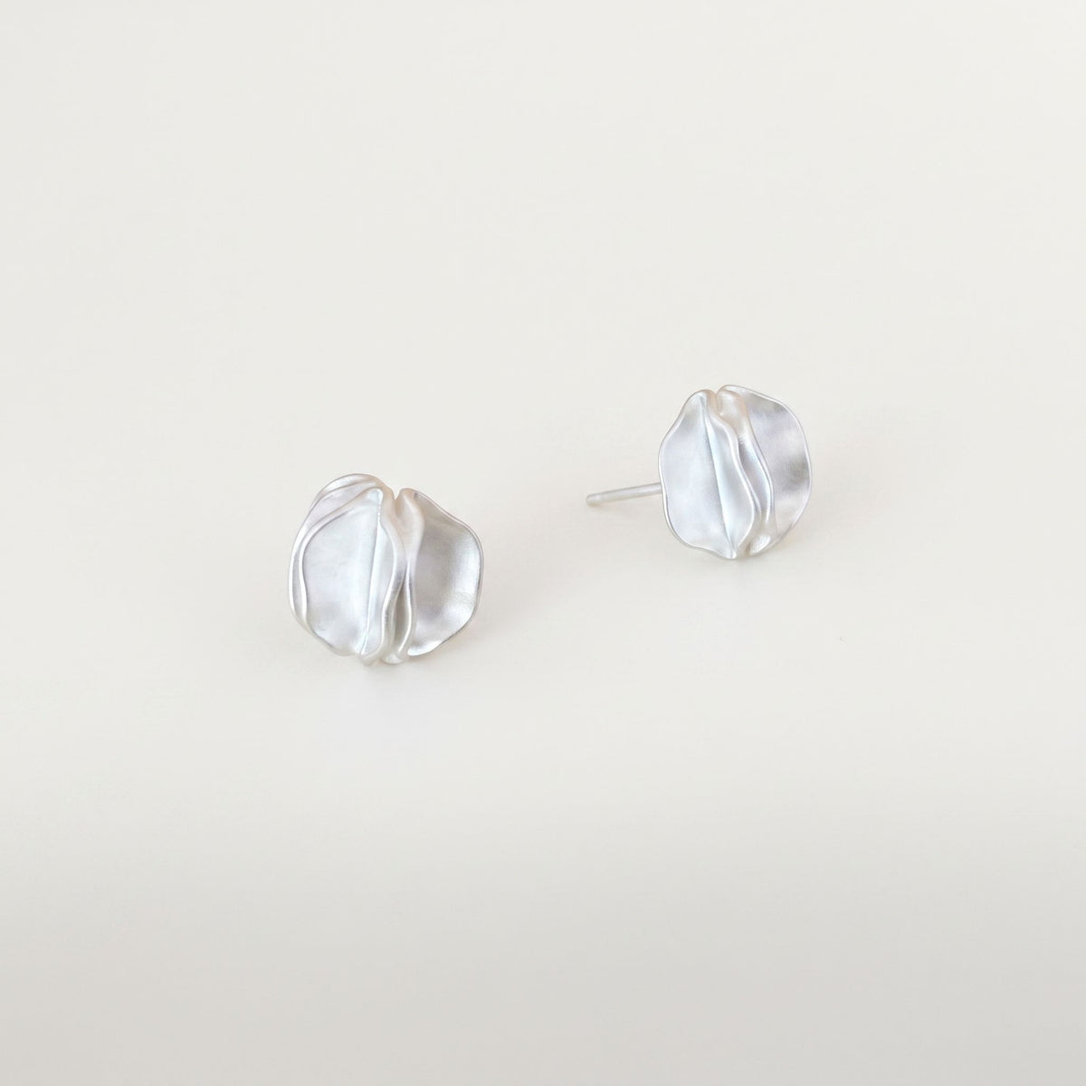 Pair of sterling silver statement stud earrings with folded petal detail on a plain near-white background