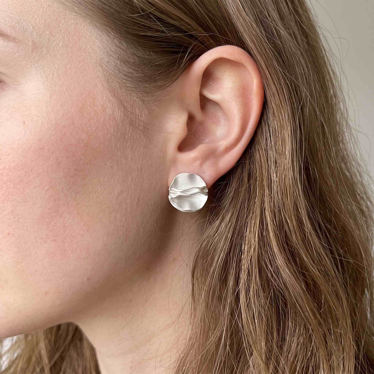 Sterling silver folded petal stud earring worn on a model's ear, showing its size against the lobe