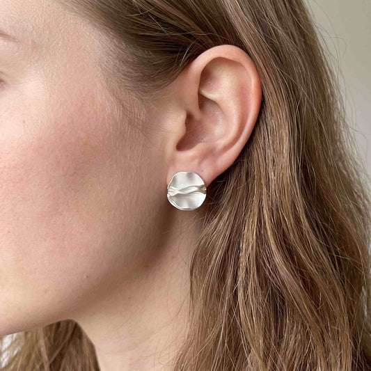 Sterling silver folded petal stud earring worn on a model's ear, showing its size against the lobe