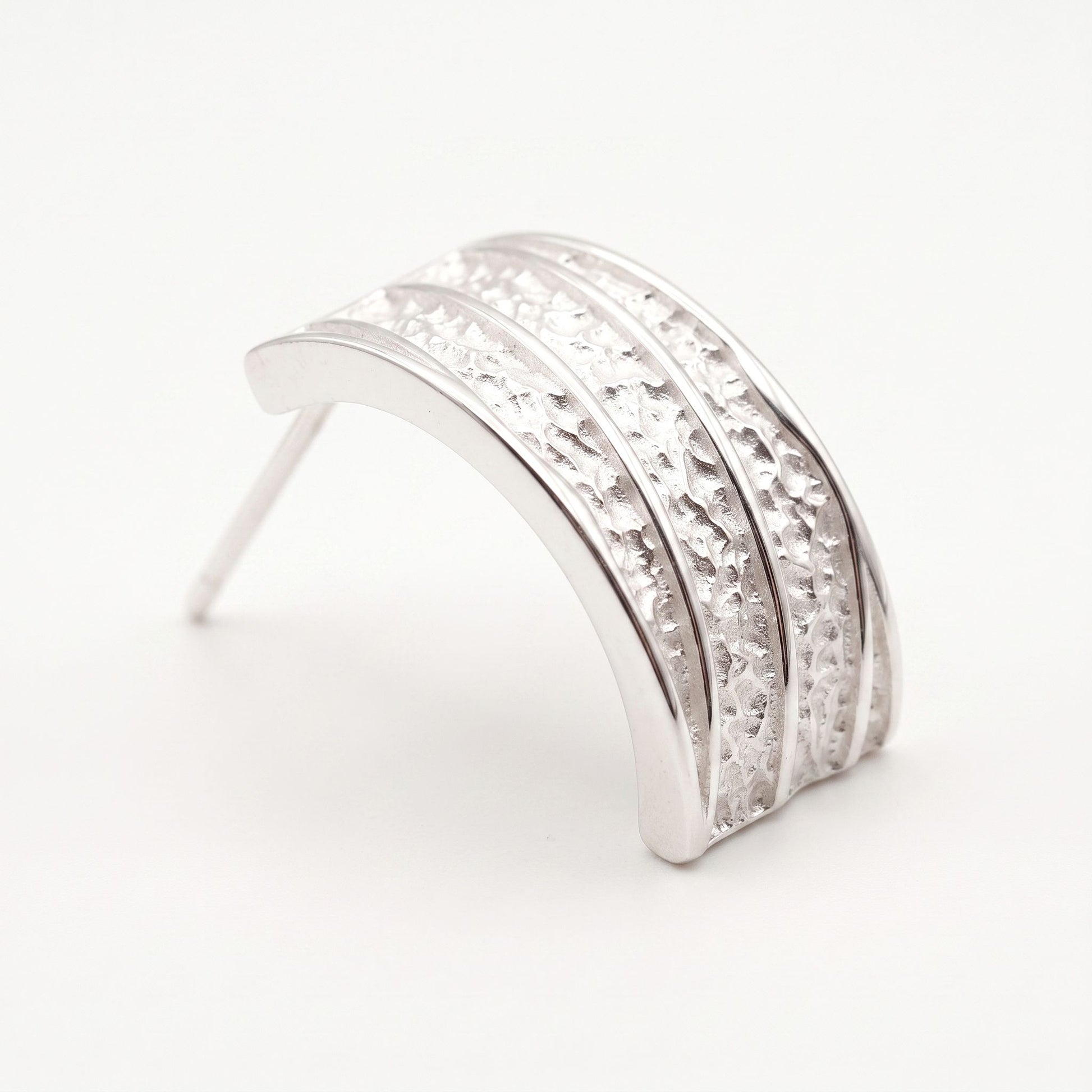 Close view of a sterling silver hammered hoop earring showing textured channels between high polish ribs
