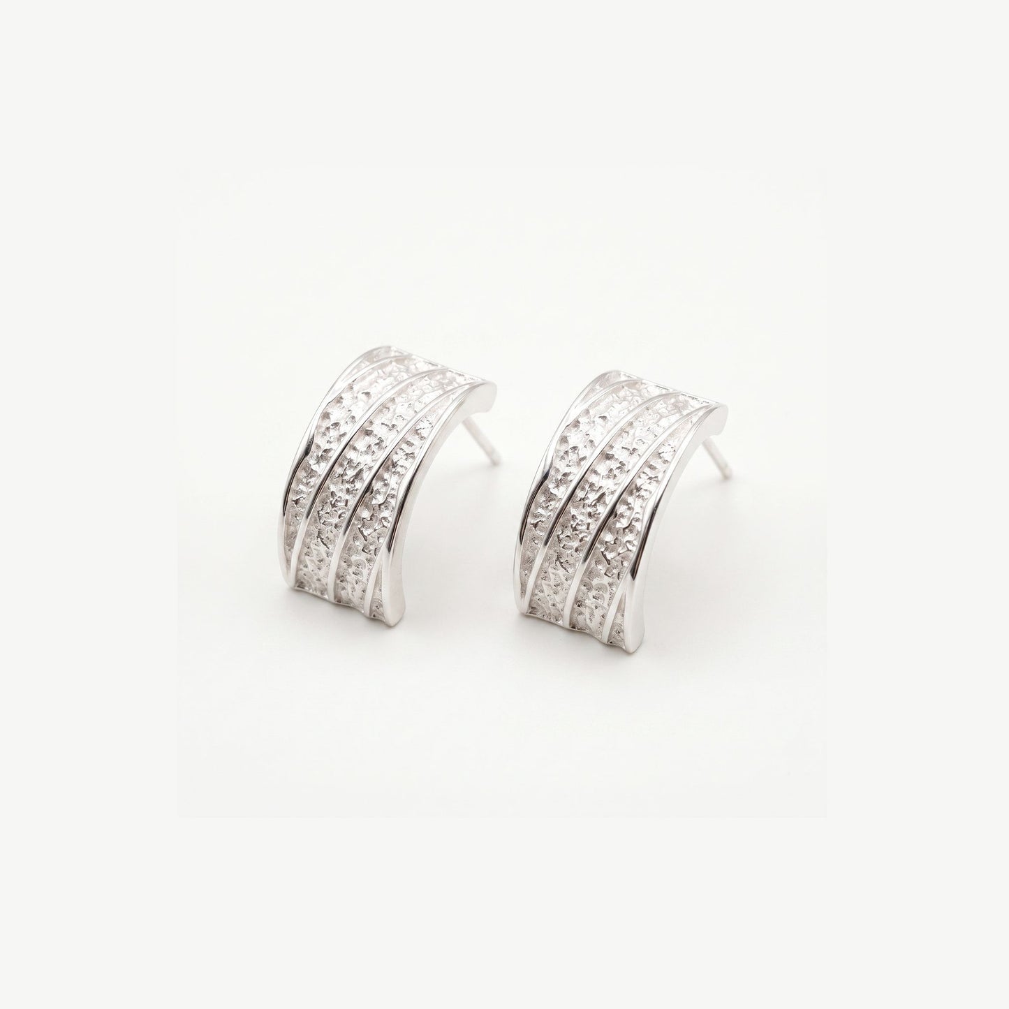 Pair of chunky sterling silver hammered half hoop earrings with polished ribs, shown on a plain white background