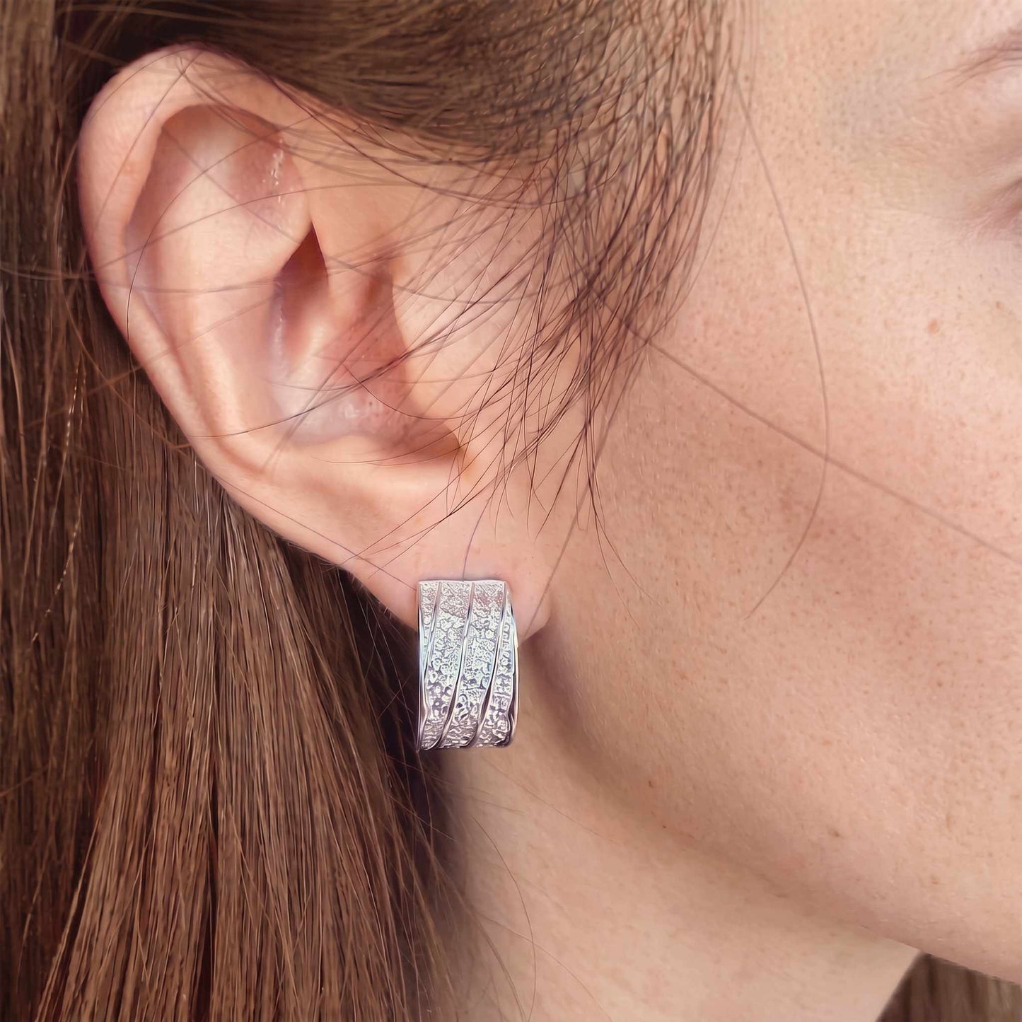Woman wearing a chunky sterling silver hammered half hoop earring on her lobe, shown for scale