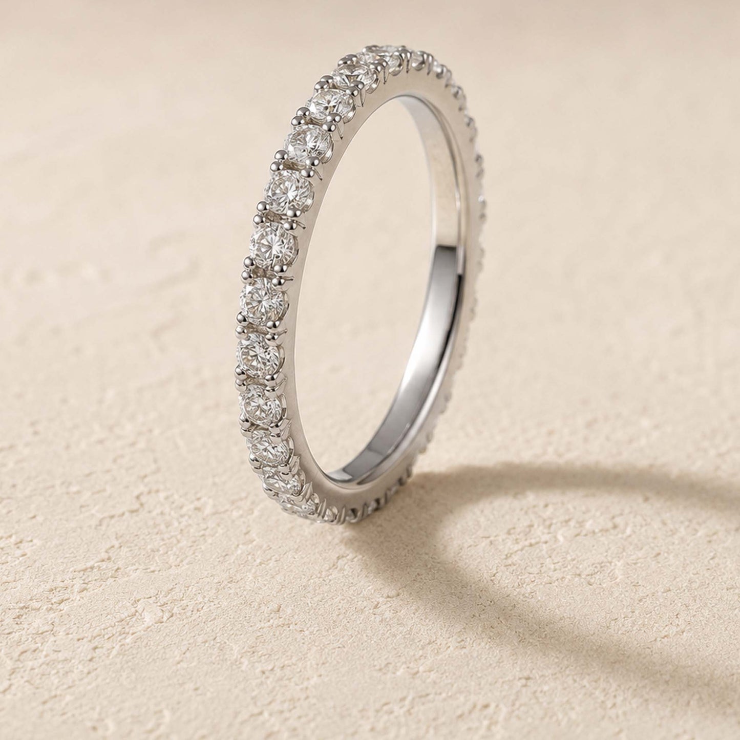 Sterling silver moissanite eternity ring standing on cream surface, micro-pavé band detail visible