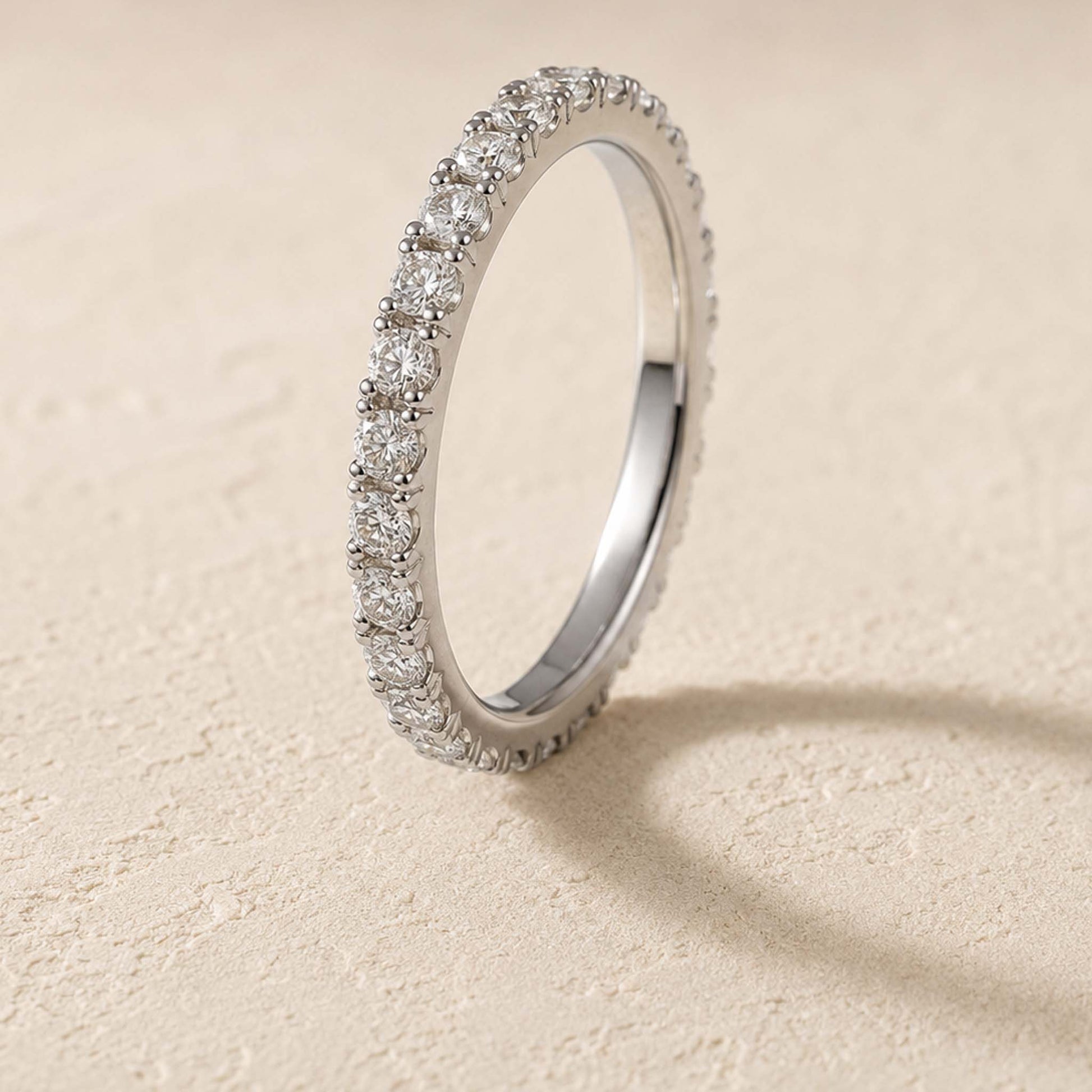 Sterling silver moissanite eternity ring standing on cream surface, micro-pavé band detail visible